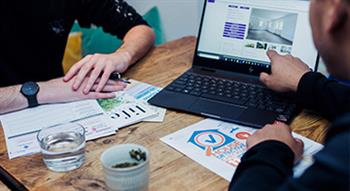 Photo of a male's hand pointing to a laptop with housing advert on screen. And another male's hands crossed and resting