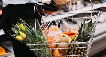 Person holding a shopping basket filled with fruit
