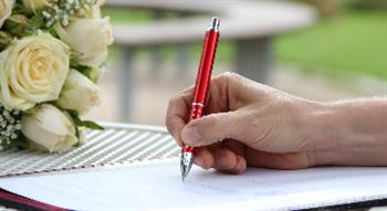 Photo of hand signing paper, wedding flowers in background