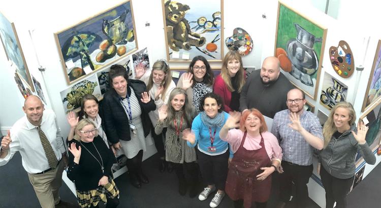 A group of teachers stand in front of artwork they have produced