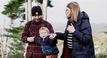 Photo of family mum, dad and young boy walking with winter coats on and trees in the background