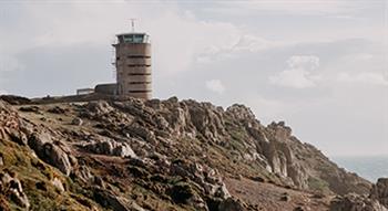 Photo of cliff headland with old german radio tower, sea in background with patchy sunshine and clouds 