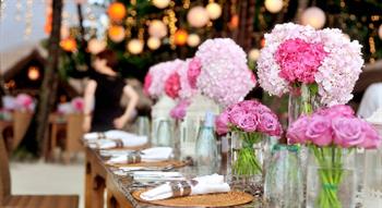Photo of row of pink and white flowers in vases at a laid table